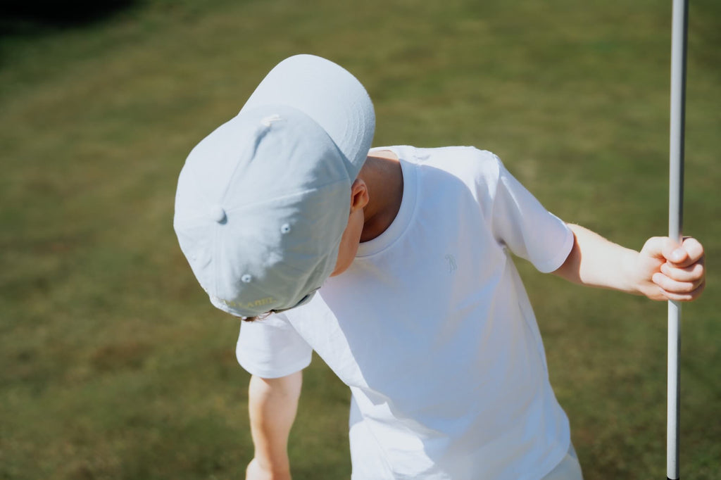 Child wearing white tee on a golf course.