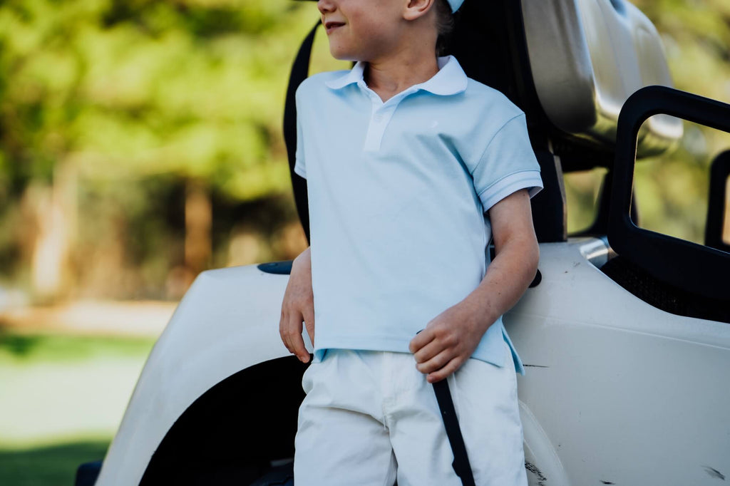 Child wearing a light blue polo shirt leaning against a golf cart.