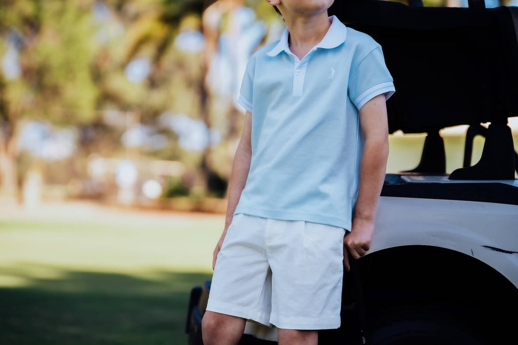 Child wearing a light blue polo shirt leaning against a golf cart.
