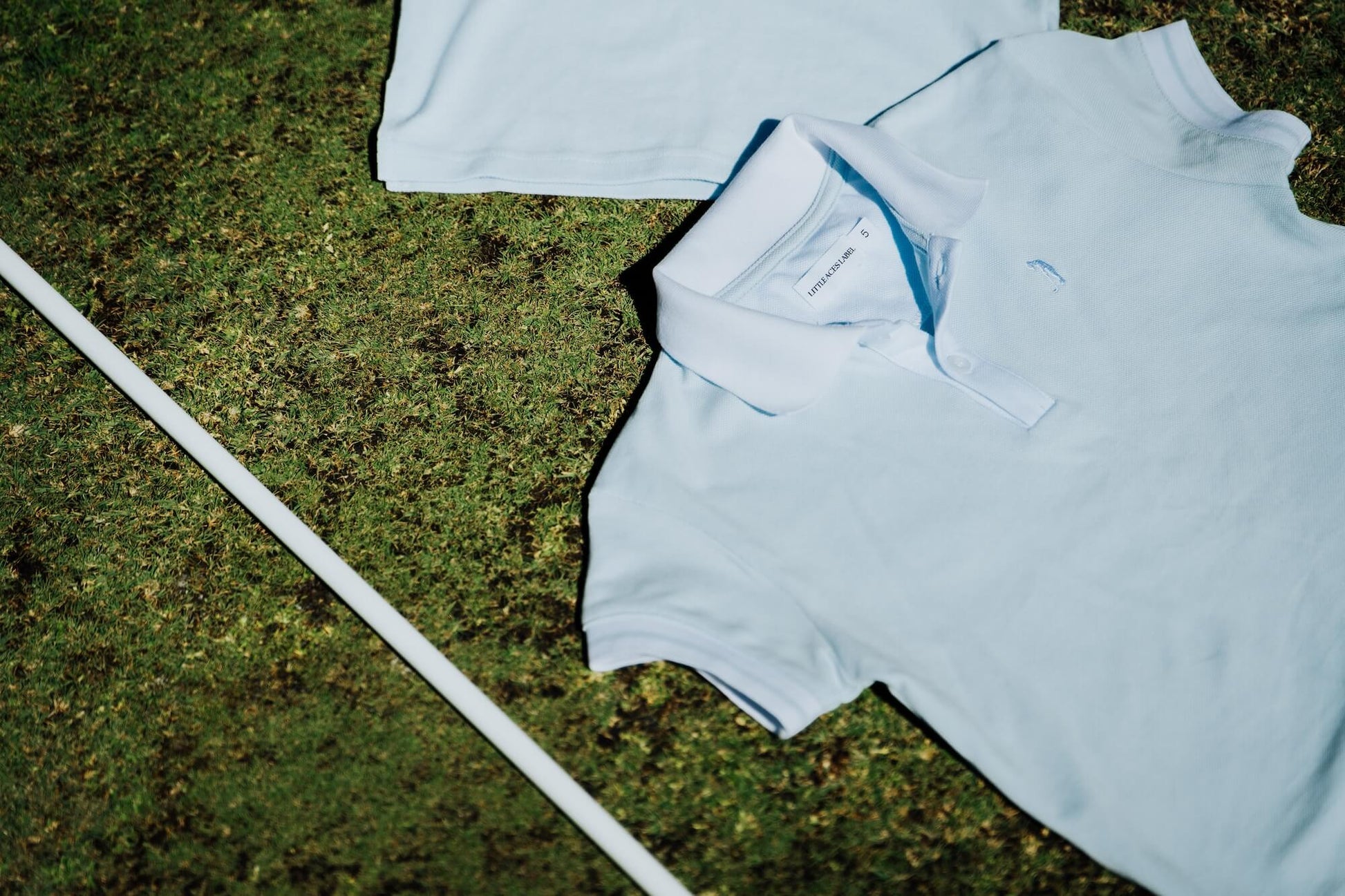 Light blue polo shirt on grass with a white golf club
