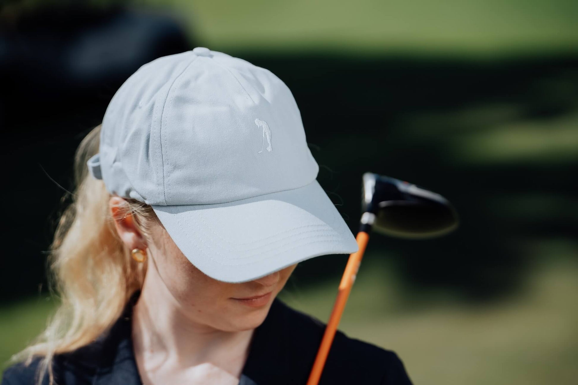 Person wearing a light blue cap holding a golf club on a blurred green background