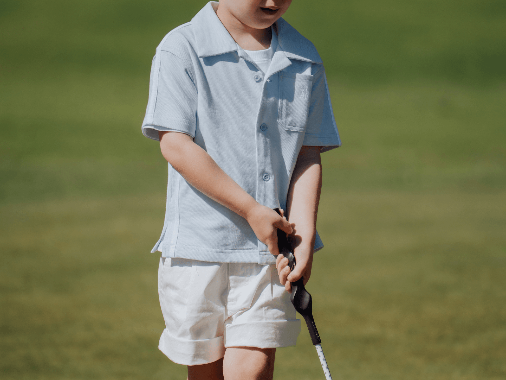 Child wearing blue button up shirt and playing golf.