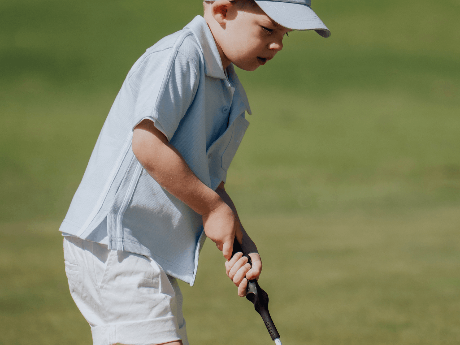 Child wearing blue button up shirt and matching blue cap and playing golf.