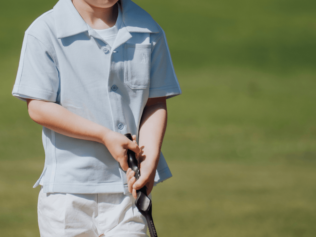 Child wearing blue button up shirt and playing golf.