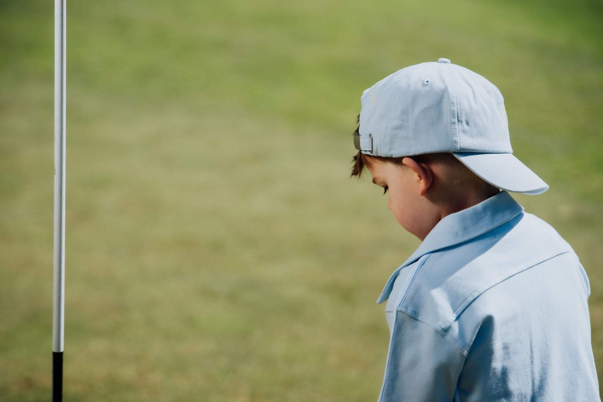 Child wearing blue button up shirt and matching blue cap and playing golf.