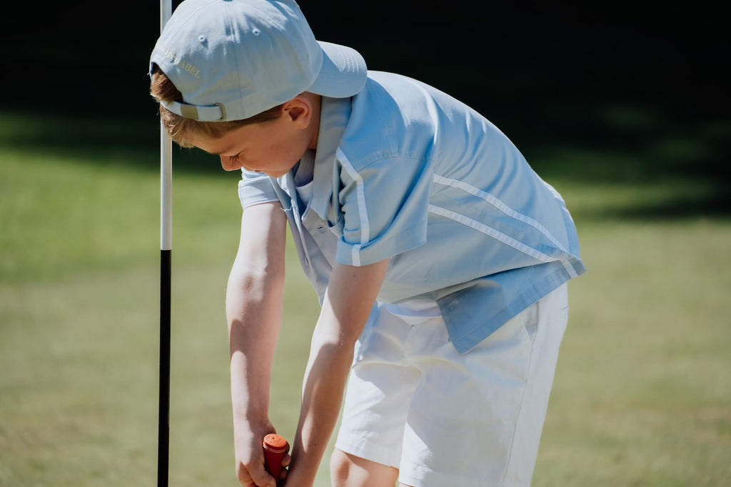 Child wearing blue button up and matching blue cap and playing golf.