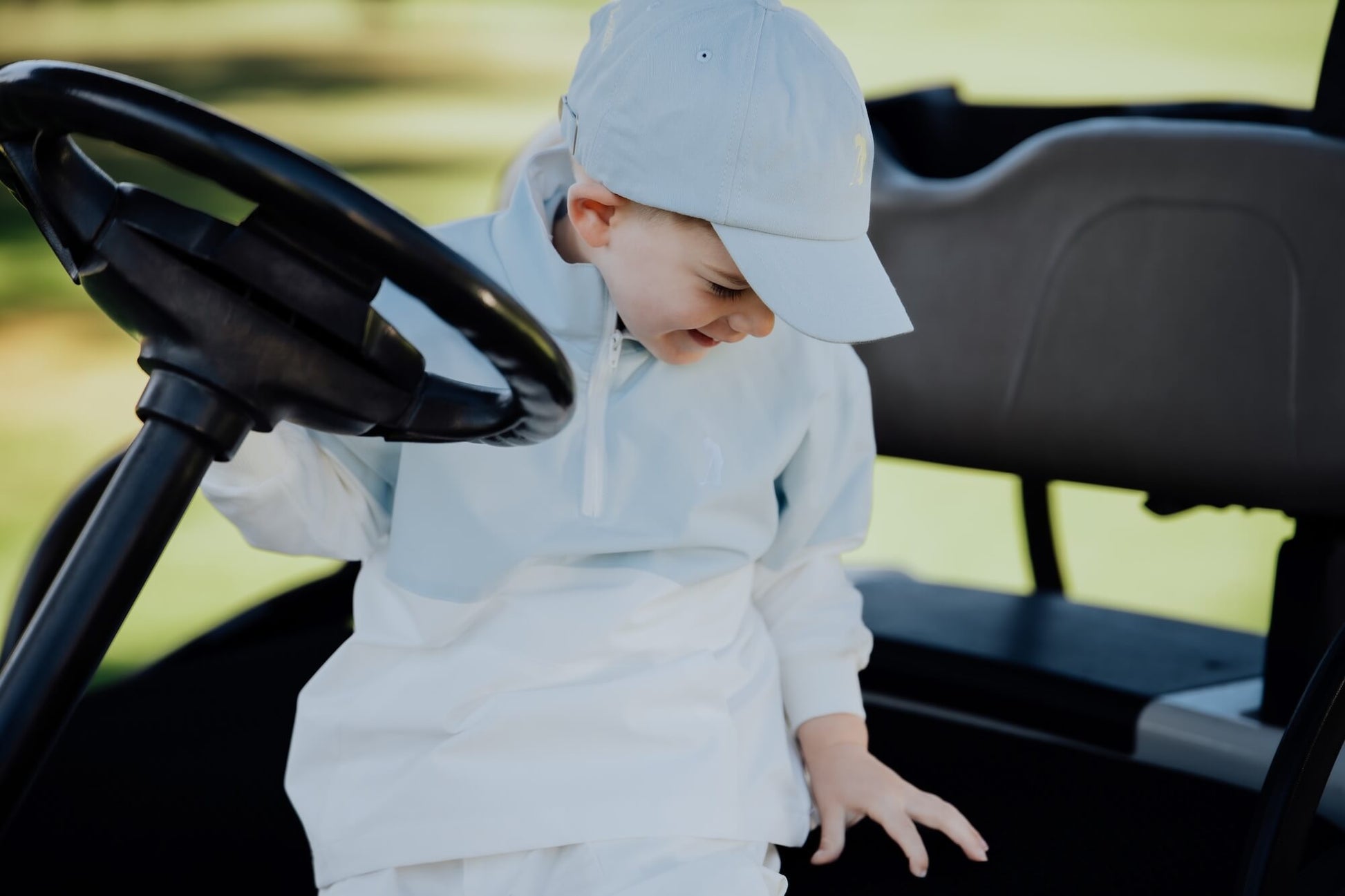 Child in block style blue and white windbreaker on golf cart.