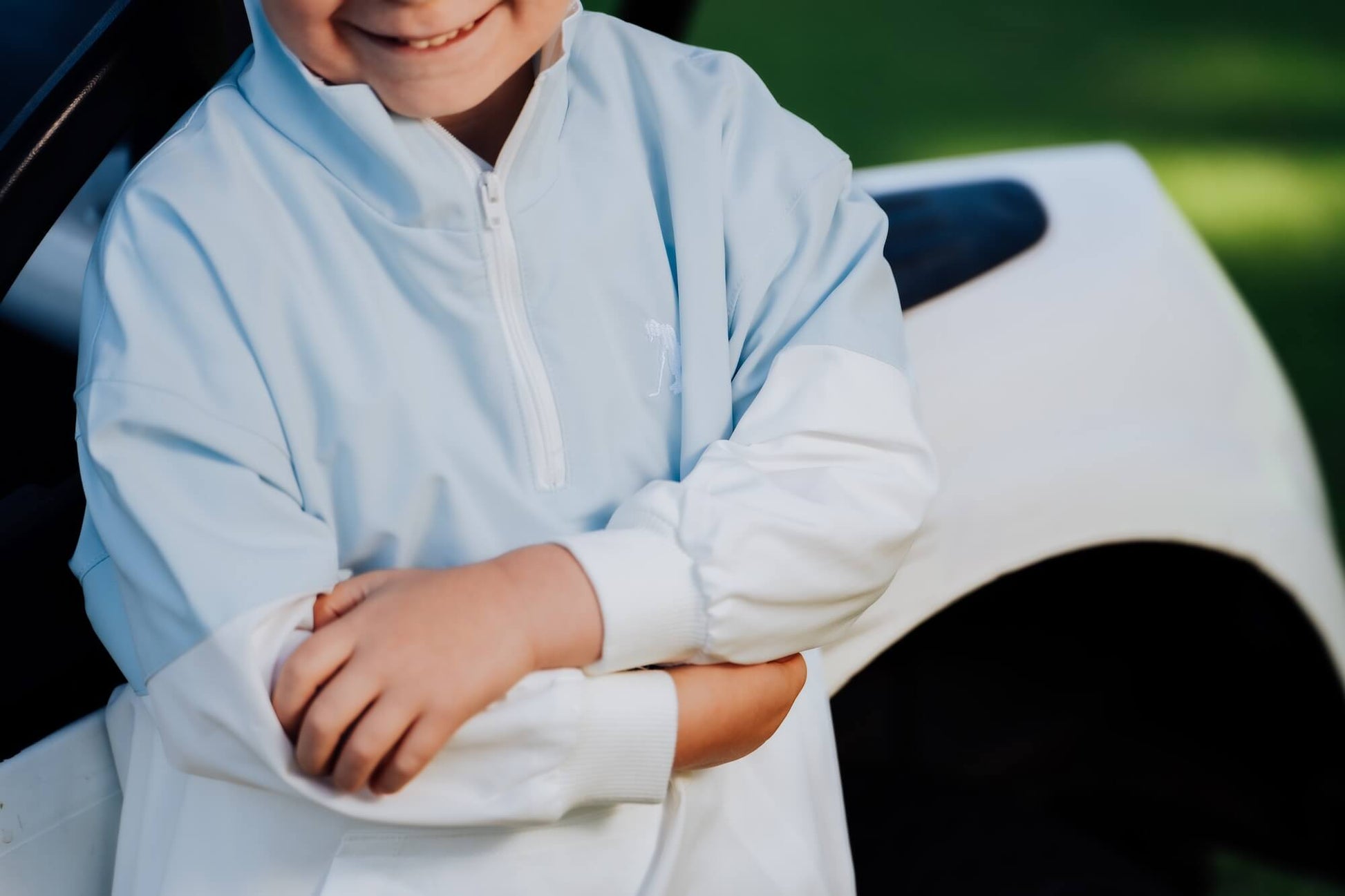 Child in block style blue and white windbreaker leaning against golf cart.