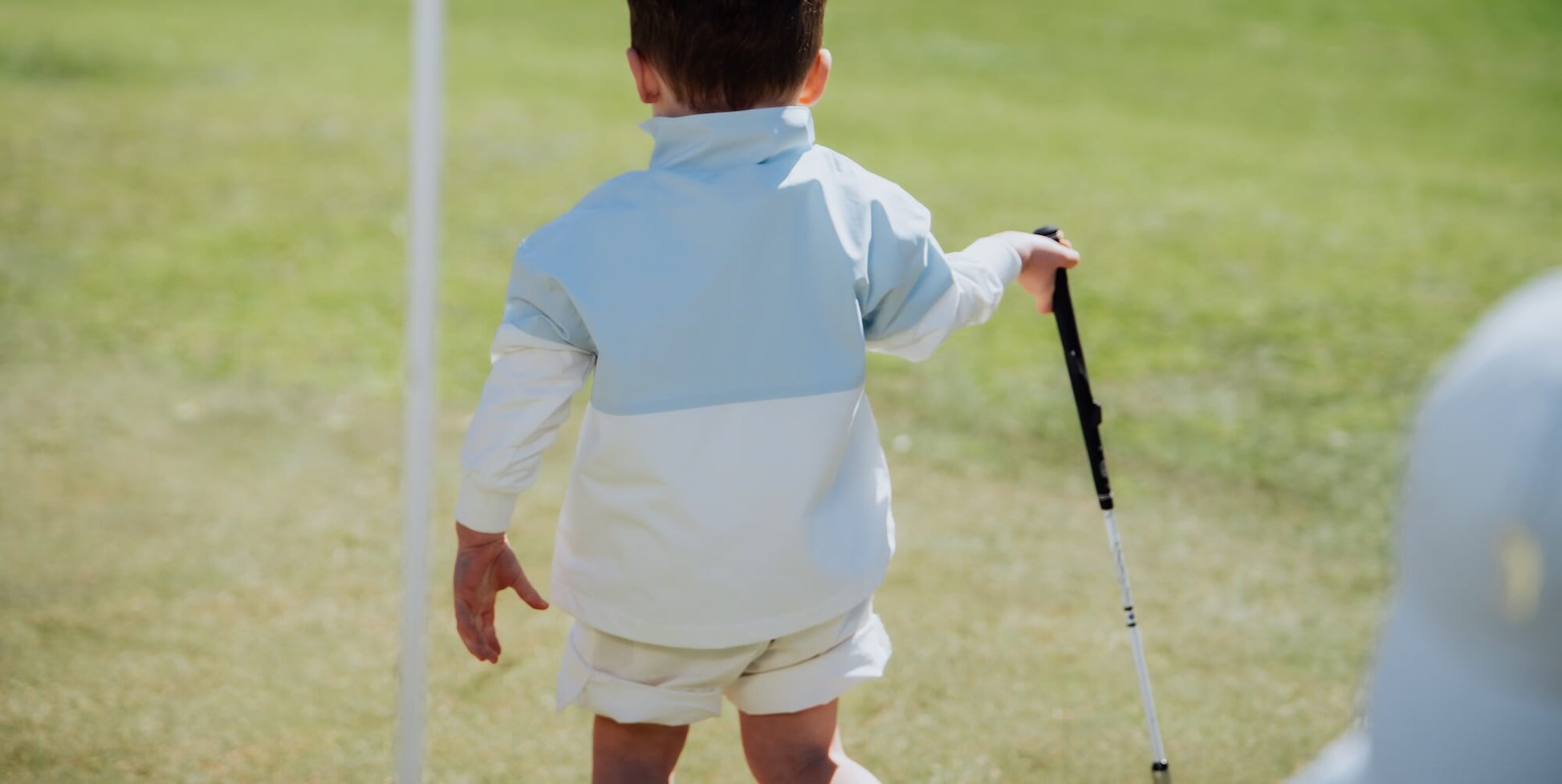 Child in block style blue and white windbreaker playing golf.