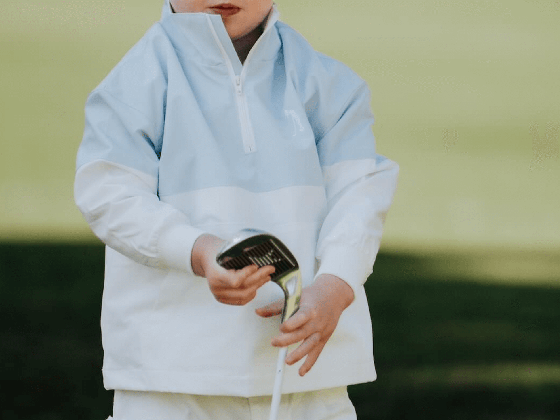 Child in block style blue and white windbreaker playing golf.