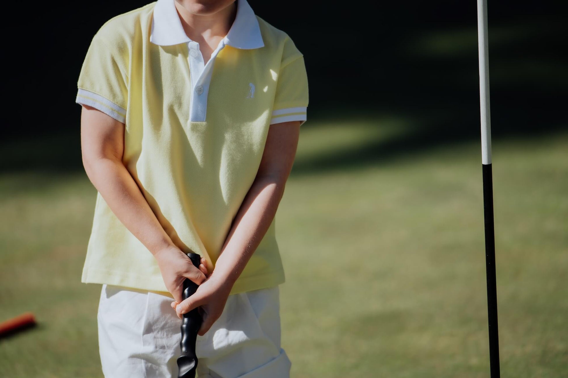 Child wearing yellow polo and playing golf.