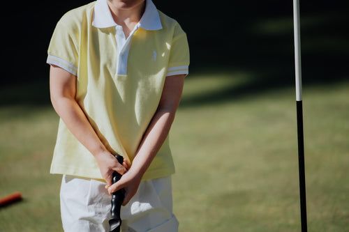Child wearing yellow polo and playing golf.