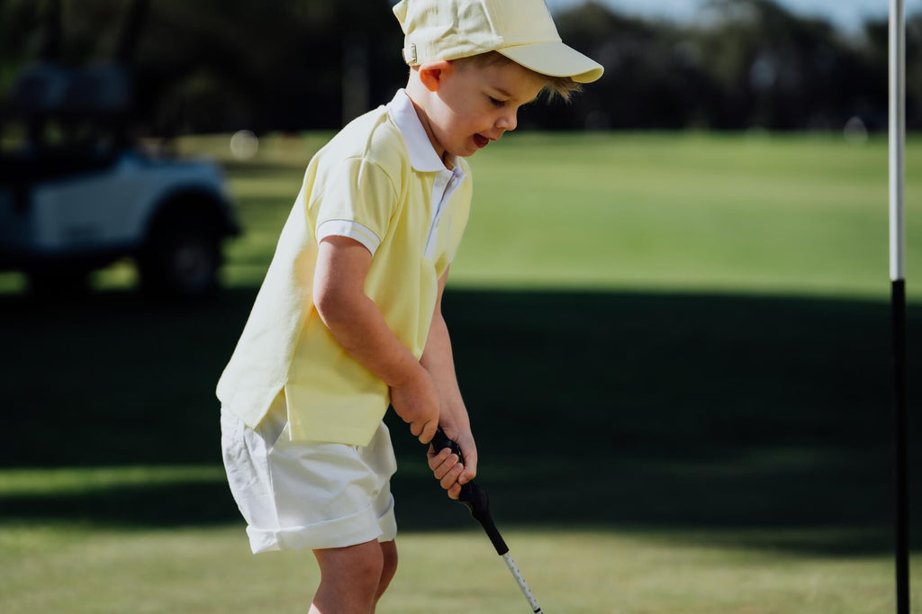Child wearing yellow polo and matching yellow cap and playing golf.