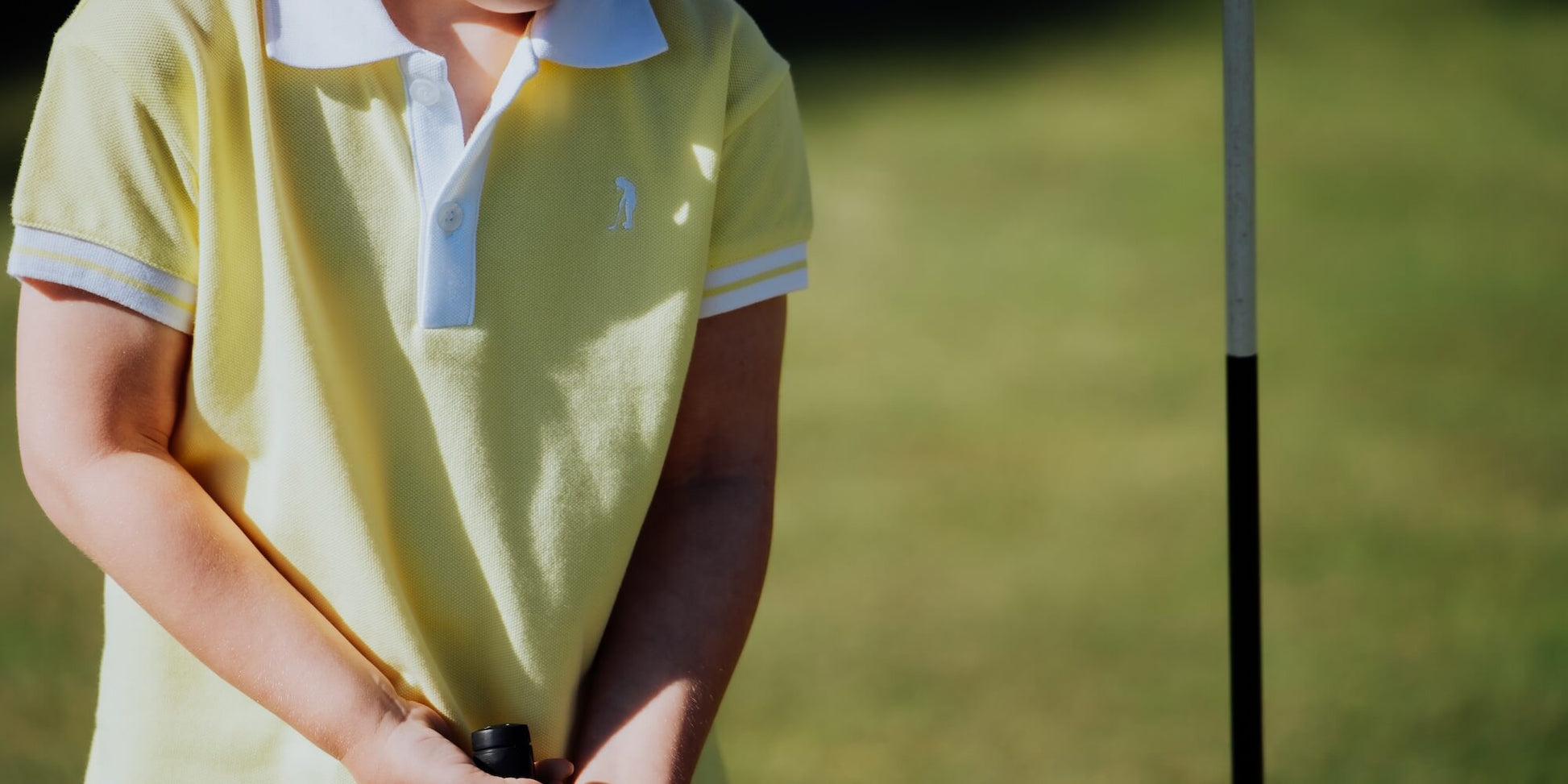 Child wearing yellow polo and playing golf.