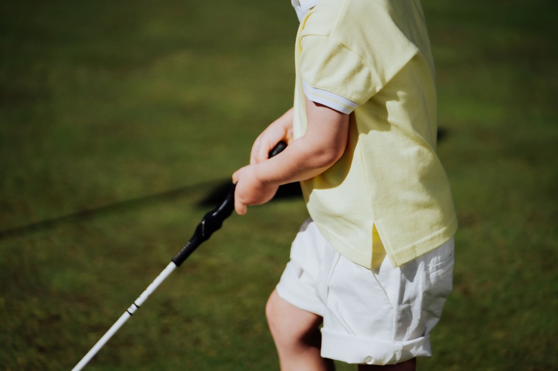 Child wearing yellow polo and playing golf.