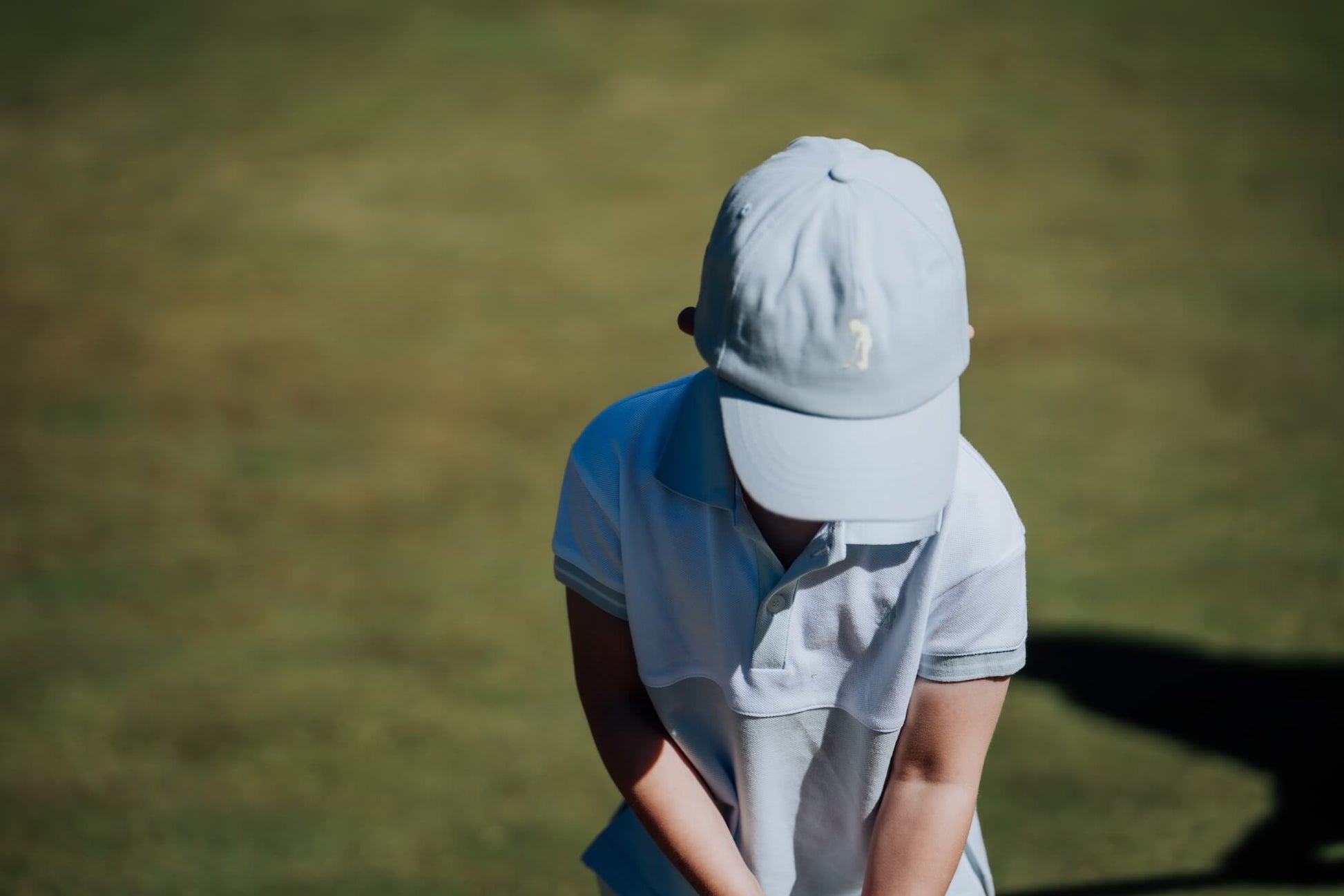 Child wearing blue and white polo and matching blue cap and playing golf.