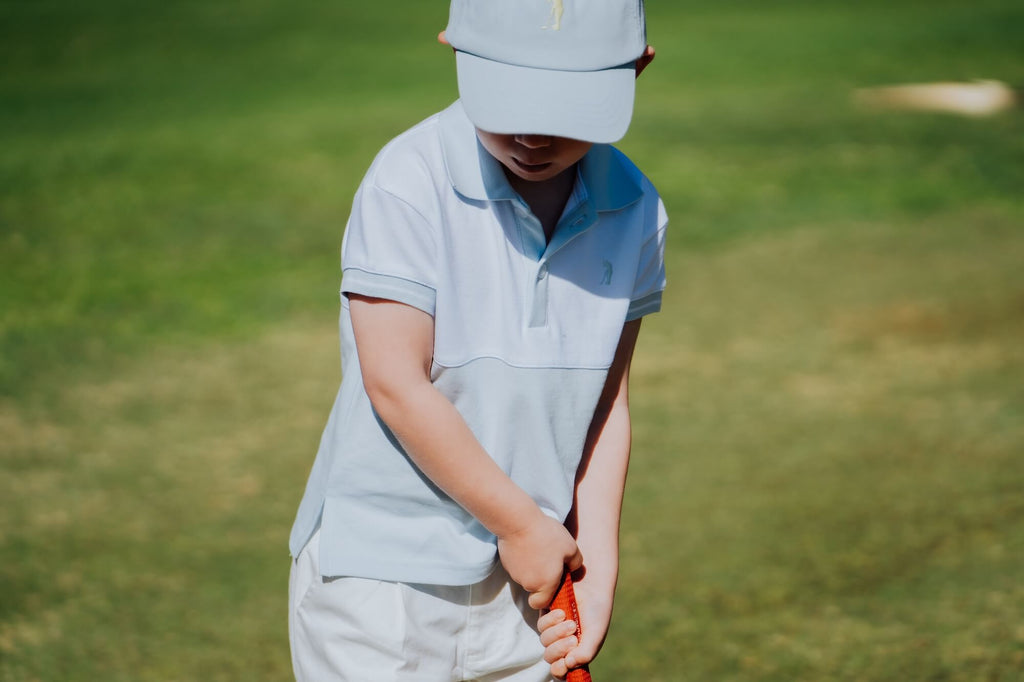 Child wearing blue and white polo and matching blue cap and playing golf.