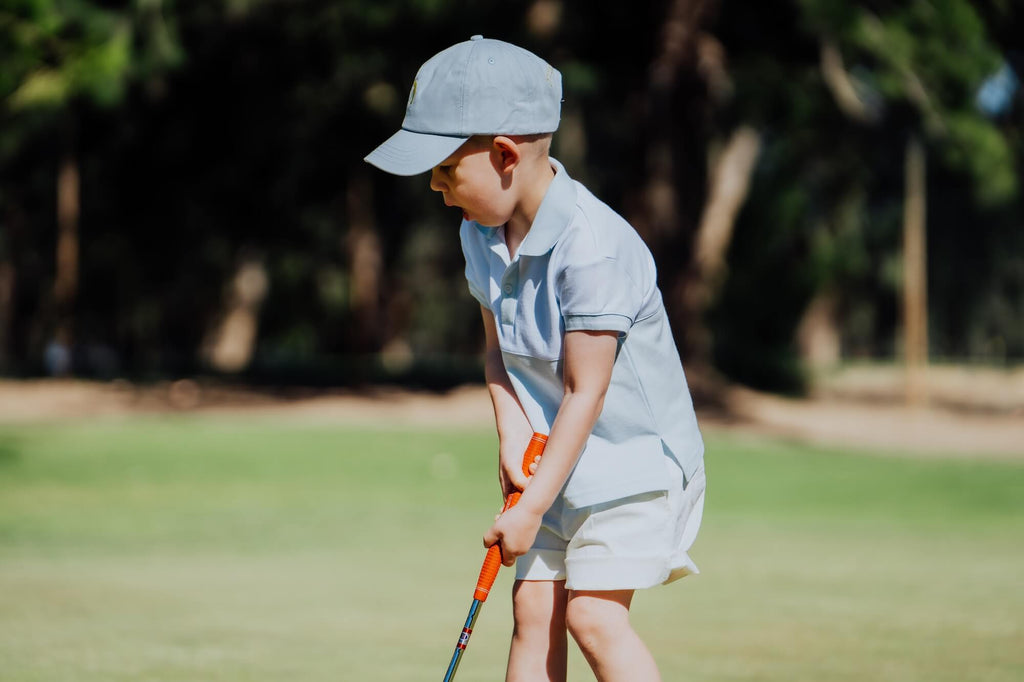 Child wearing blue and white polo and matching blue cap and playing golf.