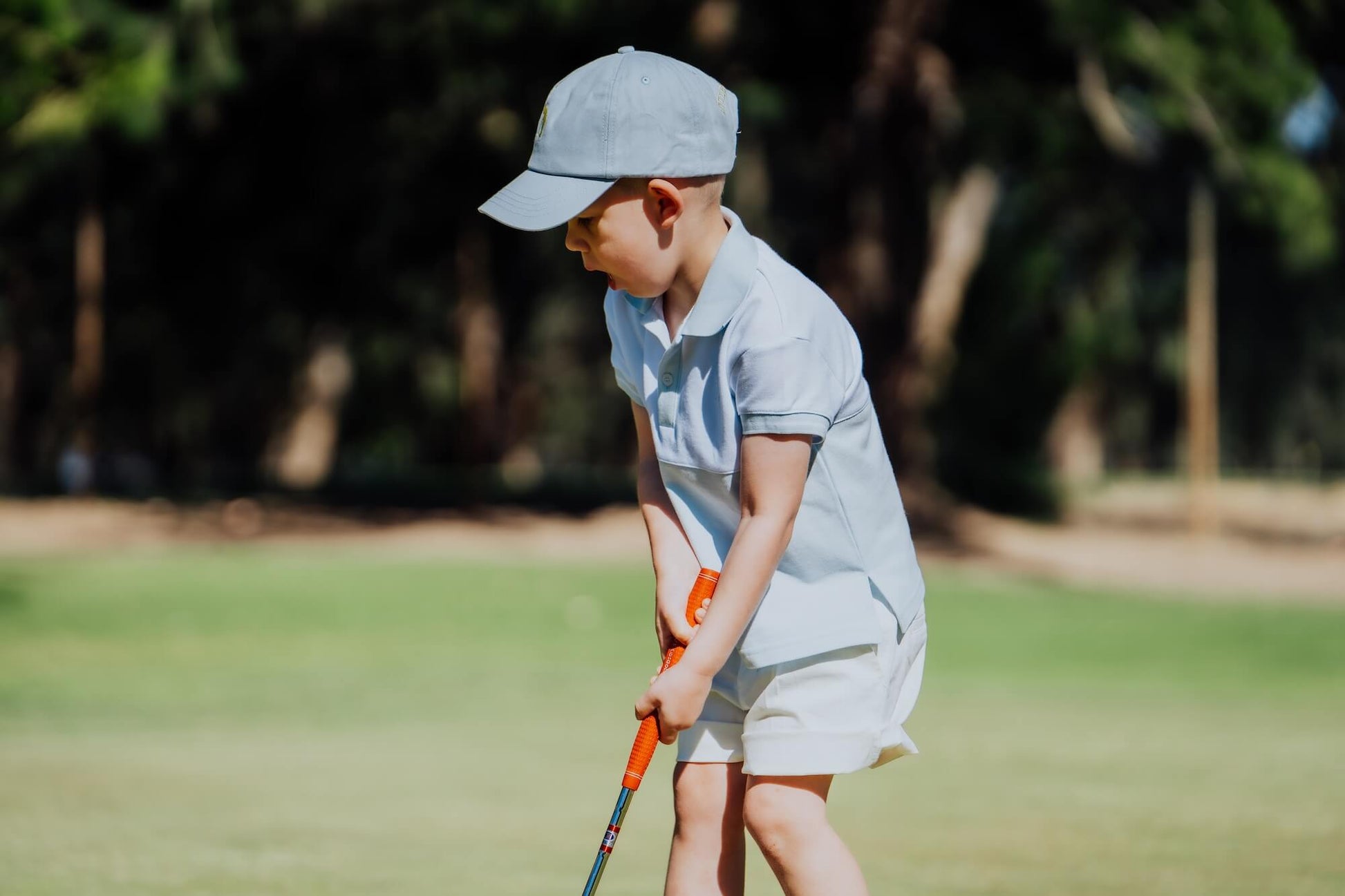 Child wearing blue and white polo and matching blue cap and playing golf.